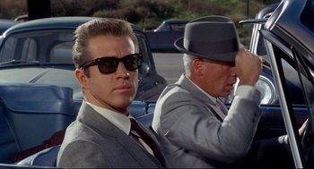 Movie still from “The Killers” (1964), directed by Don Siegel – A man in a suit and a man in a hat and sunglasses; Close Up shot, Low angle