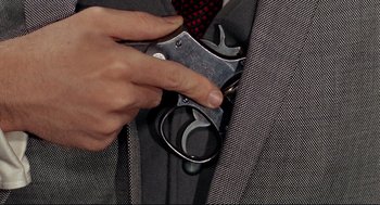 Movie still from “The Killers” (1964), directed by Don Siegel – A person holding a gun in a suit pocket; Extreme Close Up shot, Overhead angle