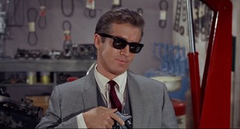 Movie still from “The Killers” (1964), directed by Don Siegel – A man in a suit and sunglasses holding a camera; Close Up shot, Low angle
