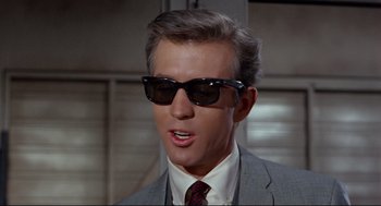 Movie still from “The Killers” (1964), directed by Don Siegel – A person wearing a suit and sunglasses; Close Up shot, Low angle