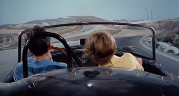 Movie still from “The Killers” (1964), directed by Don Siegel – A man and a woman driving a car in the road; Wide shot, High angle