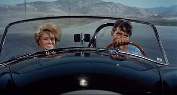 Movie still from “The Killers” (1964), directed by Don Siegel – A man and a woman driving a car in the road; Medium shot, Low angle