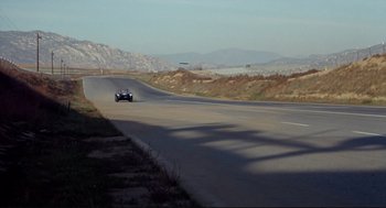 Movie still from “The Killers” (1964), directed by Don Siegel – A car driving down a road near some mountains; Extreme Wide shot, High angle