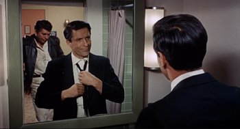 Movie still from “The Killers” (1964), directed by Don Siegel – A man looking at himself in the mirror while putting on a tie; Medium shot, Over the shoulder angle