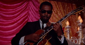 Movie still from “The Killers” (1964), directed by Don Siegel – A man in a suit and sunglasses holding a guitar; Close Up shot, Low angle