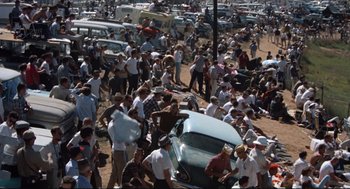 Movie still from “The Killers” (1964), directed by Don Siegel – A large group of people standing around parked cars; Extreme Wide shot, High angle