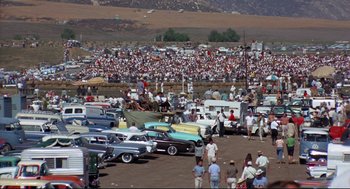 Movie still from “The Killers” (1964), directed by Don Siegel – A crowd of people standing around a parking lot; Extreme Wide shot, High angle