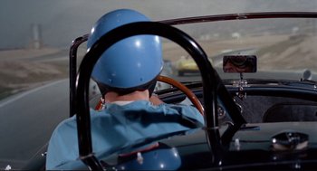 Movie still from “The Killers” (1964), directed by Don Siegel – A person in a blue helmet driving a car; Medium shot, Over the shoulder angle