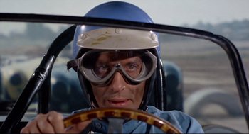 Movie still from “The Killers” (1964), directed by Don Siegel – A man wearing goggles and a helmet while driving a car; Close Up shot, Low angle
