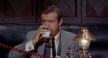 Movie still from “The Killers” (1964), directed by Don Siegel – A man in a gray suit drinking a glass of milk; Close Up shot, High angle