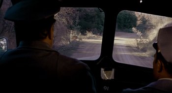 Movie still from “The Killers” (1964), directed by Don Siegel – A man riding in the back of a vehicle; Wide shot, High angle