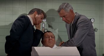 Movie still from “The Killers” (1964), directed by Don Siegel – Three men in suits are looking at a man's head in a chair; Medium shot, High angle