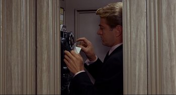 Movie still from “The Killers” (1964), directed by Don Siegel – A man in a black suit and white shirt holding a phone; Medium shot, Low angle