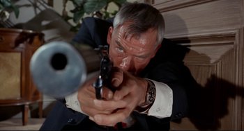 Movie still from “The Killers” (1964), directed by Don Siegel – An older man in a suit and tie holding a gun; Close Up shot, Low angle