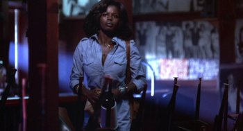 Movie still from “The Killing of a Chinese Bookie” (1976), directed by John Cassavetes – A woman standing in a room holding a bottle of wine; Medium shot, Low angle