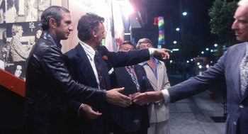 Movie still from “The Killing of a Chinese Bookie” (1976), directed by John Cassavetes – A group of men standing next to each other on a sidewalk; Medium shot, Over the shoulder angle