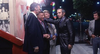 Movie still from “The Killing of a Chinese Bookie” (1976), directed by John Cassavetes – A group of men standing next to each other on a sidewalk; Medium shot, Low angle