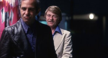 Movie still from “The Killing of a Chinese Bookie” (1976), directed by John Cassavetes – A man in a suit and tie standing next to another man in a suit and tie; Medium shot, Over the shoulder angle