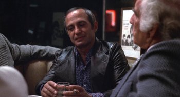 Movie still from “The Killing of a Chinese Bookie” (1976), directed by John Cassavetes – A man sitting in front of another man holding a drink; Medium shot, Over the shoulder angle