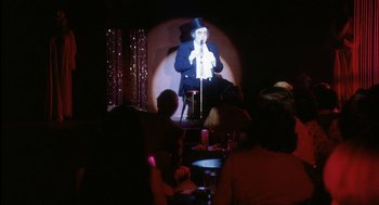 Movie still from “The Killing of a Chinese Bookie” (1976), directed by John Cassavetes – A man in a top hat is on a stage; Wide shot, Over the shoulder angle