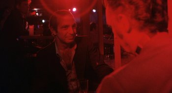 Movie still from “The Killing of a Chinese Bookie” (1976), directed by John Cassavetes – A man sitting at a table with a cigarette in his mouth; Medium shot, Over the shoulder angle