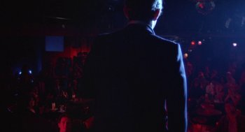 Movie still from “The Killing of a Chinese Bookie” (1976), directed by John Cassavetes – A man in a suit standing in front of a crowd; Wide shot, Over the shoulder angle