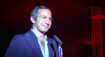Movie still from “The Killing of a Chinese Bookie” (1976), directed by John Cassavetes – A man in a blue suit standing in front of a microphone; Close Up shot, High angle