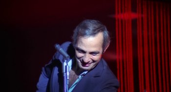 Movie still from “The Killing of a Chinese Bookie” (1976), directed by John Cassavetes – A man in a black suit is holding a microphone; Close Up shot, High angle