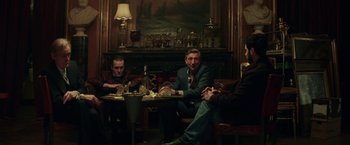 Movie still from “The Kindness of Strangers” (2019), directed by Lone Scherfig – A group of men sitting at a table in front of a fireplace; Wide shot, Low angle