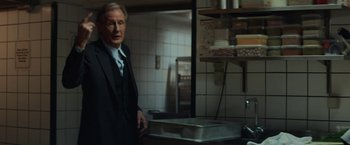 Movie still from “The Kindness of Strangers” (2019), directed by Lone Scherfig – A man in a suit standing in a kitchen next to a sink; Medium shot, Over the shoulder angle