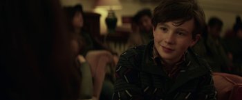 Movie still from “The Kindness of Strangers” (2019), directed by Lone Scherfig – A young man sitting in a room with other people in the background; Close Up shot, Over the shoulder angle
