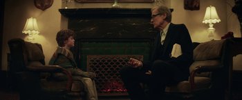 Movie still from “The Kindness of Strangers” (2019), directed by Lone Scherfig – A man and a boy sitting in front of a fireplace; Medium shot, Over the shoulder angle
