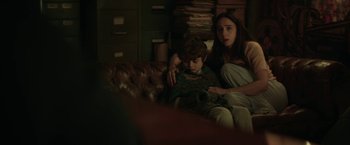 Movie still from “The Kindness of Strangers” (2019), directed by Lone Scherfig – A woman and a boy sitting on top of a brown couch; Medium shot, Over the shoulder angle