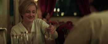 Movie still from “The Kindness of Strangers” (2019), directed by Lone Scherfig – A woman sitting at a table holding a wine glass; Medium shot, Over the shoulder angle