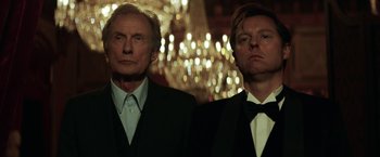 Movie still from “The Kindness of Strangers” (2019), directed by Lone Scherfig – A man and a man standing next to each other in front of a chandelier; Close Up shot, Low angle