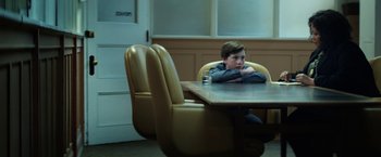 Movie still from “The Kindness of Strangers” (2019), directed by Lone Scherfig – A boy sitting at a dining room table with a glass of water; Medium shot, Over the shoulder angle