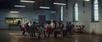 Movie still from “The Kindness of Strangers” (2019), directed by Lone Scherfig – A group of people sitting in a circle in a room; Wide shot, High angle