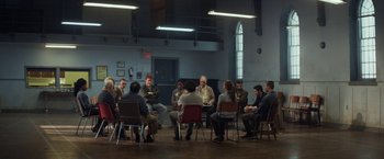 Movie still from “The Kindness of Strangers” (2019), directed by Lone Scherfig – A group of people sitting around a room together; Wide shot, High angle