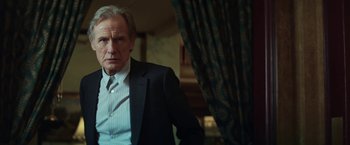 Movie still from “The Kindness of Strangers” (2019), directed by Lone Scherfig – A man wearing a suit and tie standing in front of a curtain; Medium shot, Low angle