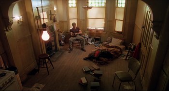 Movie still from “Good Will Hunting” (1997), directed by Gus Van Sant – A man sitting on a chair in a messy room; Wide shot, High angle