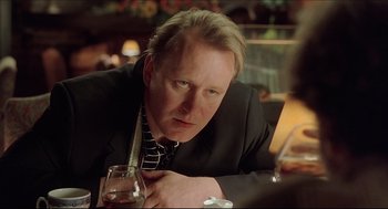 Movie still from “Good Will Hunting” (1997), directed by Gus Van Sant – A man sitting at a table with a glass of wine; Close Up shot, Over the shoulder angle