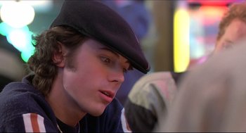 Movie still from “Good Will Hunting” (1997), directed by Gus Van Sant – A young man wearing a black hat looking at something on a table; Close Up shot, Over the shoulder angle
