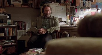 Movie still from “Good Will Hunting” (1997), directed by Gus Van Sant – A man sitting at a desk in front of books; Medium shot, Over the shoulder angle
