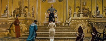 Movie still from “The King and I” (1956), directed by Walter Lang – A man sitting on top of a chair in front of a woman; Wide shot, Low angle
