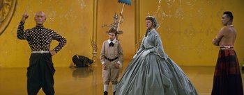 Movie still from “The King and I” (1956), directed by Walter Lang – A boy and a woman in a costume in front of a yellow wall; Wide shot, Low angle