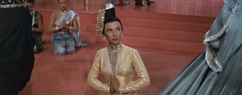 Movie still from “The King and I” (1956), directed by Walter Lang – A woman in a gold dress and a black head piece; Medium shot, Low angle