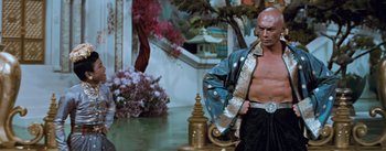 Movie still from “The King and I” (1956), directed by Walter Lang – A bald man in a blue jacket standing next to a fire hydrant; Medium shot, Low angle