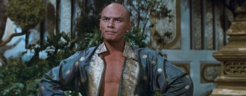Movie still from “The King and I” (1956), directed by Walter Lang – A bald man in a blue shirt is looking at the camera; Medium shot, Low angle