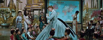 Movie still from “The King and I” (1956), directed by Walter Lang – A woman in a long blue dress standing in front of a group of people; Wide shot, High angle