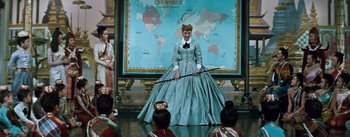 Movie still from “The King and I” (1956), directed by Walter Lang – A woman in a blue dress holding a stick in front of a group of people; Wide shot, High angle
